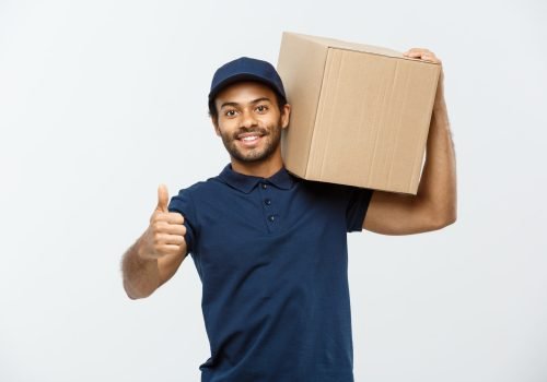 Delivery Concept - Portrait of Happy African American delivery man holding a box package and showing thumps up. Isolated on Grey studio Background. Copy Space.